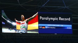 Der deutsche Weitspringer Markus Rehm jubelt auf einer Videowand über Paralympischen Rekord. © Binh Truong/DBS Foto: Binh Truong
